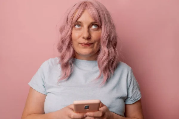 Retrato de atractiva hermosa mujer joven caucásica pensando en el uso de teléfono móvil posando aislado sobre fondo de pared rosa — Foto de Stock