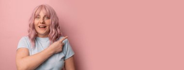 Lütfen dikkat. Mavi tişörtlü çekici beyaz kadın portresi parmak kaldırıyor, fotokopi alanını gösteriyor, pembe arka planda izole edilmiş bilgileri yayıyor.