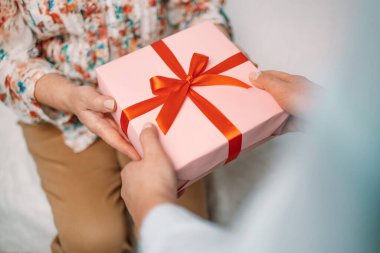 Bir kadının annesine pembe bir hediye kutusu verdiği yakın plan görüntüsü. Anneler Günün kutlu olsun, doğum günü konsepti.