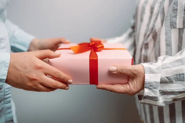 Person hand ger rosa presentförpackning med rött band till en kvinna. — Stockfoto