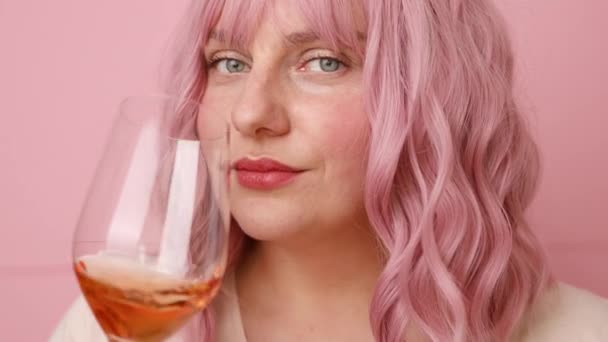 Mooie jonge vrouw drinken een glas roze wijn geïsoleerd over roze achtergrond — Stockvideo