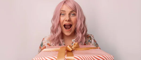 Porträt einer glücklichen verrückten jungen Frau, die in die Kamera schaut und lächelnd posiert, mit Geschenk-Box isoliert auf grauem Hintergrund — Stockfoto