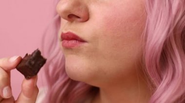 Pembe arka planda izole edilmiş çikolatalı waffle şekerini ısıran genç bir kadının portresi.