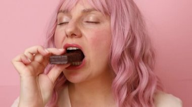 Pembe arka planda izole edilmiş çikolatalı waffle şekerini ısıran genç bir kadın.