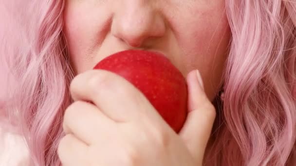 Primer plano de la joven mujer de pelo rosa comiendo manzana aislada sobre fondo rosa — Vídeos de Stock