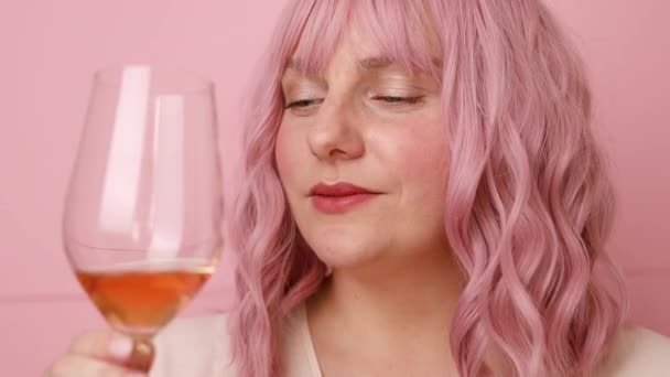 Hermosa mujer de 30 años con el pelo rizado rosa beber vino rosa sobre fondo de color rosa brillante — Vídeos de Stock