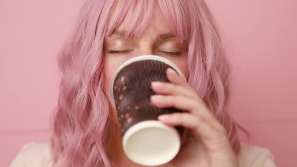 Молода красива 20-річна жінка в білій футболці тримає виносний ремісничий паперовий коричневий стаканчик і п'є каву на рожевому фоні . — стокове відео
