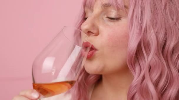Красивая женщина 30-х годов с розовыми вьющимися волосами пьет розовое вино на ярко-розовом фоне — стоковое видео