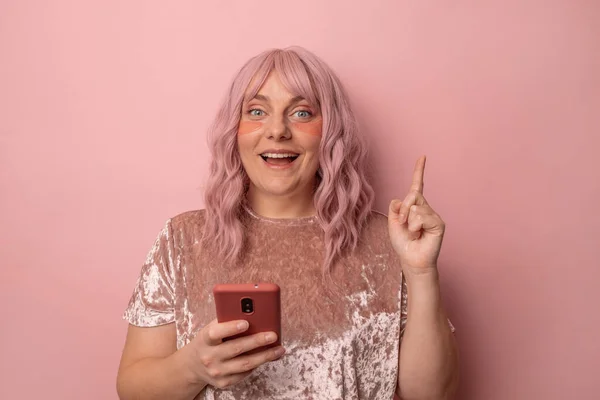 Atención, por favor. Retrato de cerca de la atractiva mujer caucásica en camiseta rosa levanta el dedo hacia arriba, mostrando el espacio de copia, la difusión de la información de fondo rosa aislado —  Fotos de Stock