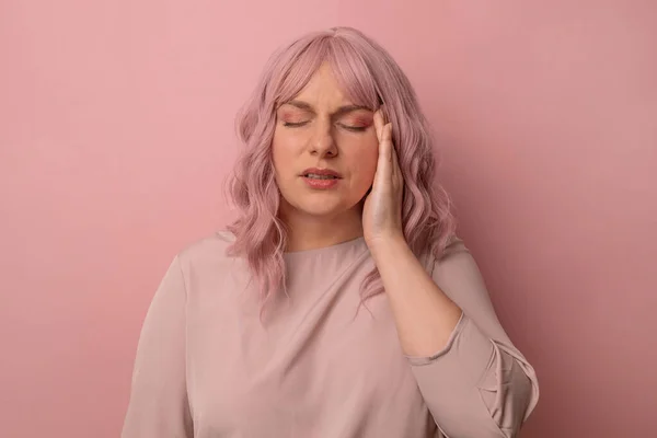 머리에 통증을 호소하기 위해 손을 들고 서 있는 30 대 여성 이 있습니다. 그 이유는 격리 된 핑크 배경때문이죠. 편두통 이 있다. 건강 과 스트레스의 개념 — 스톡 사진
