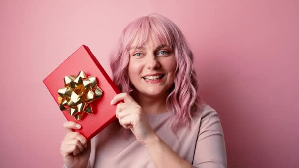 Retrato de una joven feliz y positiva en buen humor sosteniendo una caja de regalo aislada sobre fondo rosa. Vacaciones, celebración y concepto de mujer — Vídeo de stock