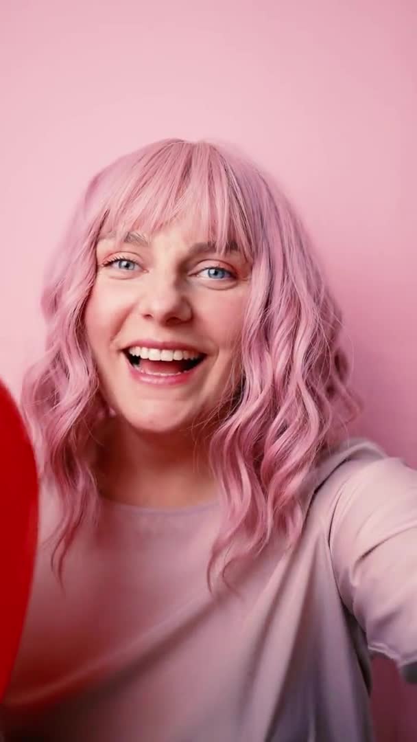 Porträtt av söt ung kvinna med hjärtform luft ballong tittar på kameran och ler medan du tar selfie foto isolerad rosa bakgrund, människor livsstil koncept — Stockvideo