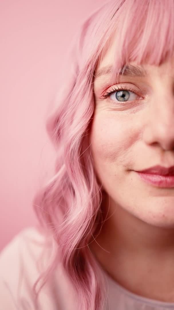 Primer plano de la cara femenina humana con el pelo rosa. Mujer con maquillaje de belleza facial natural mirando a la cámara aislada sobre fondo rosa — Vídeos de Stock