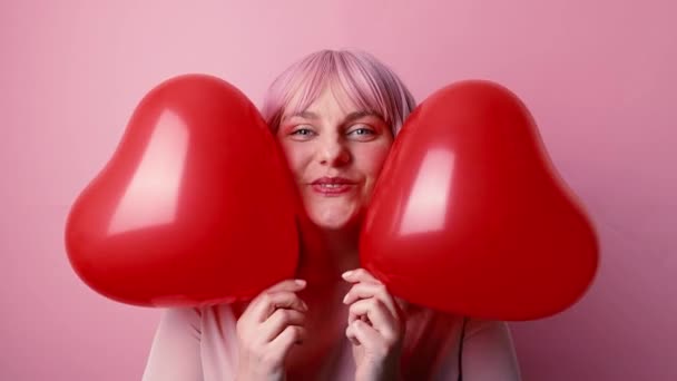 Felice bella donna di buon umore sorridente tenendo palloncini d'aria cuore a forma di rosso celebra compleanno isolato su sfondo rosa. — Video Stock