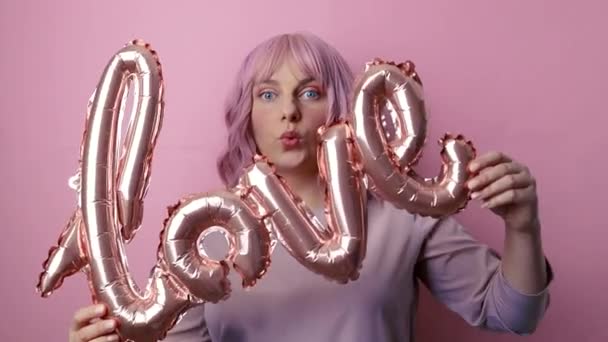 Walentynki. Dość młoda kobieta po trzydziestce dobrze się bawiąc trzymając różową folię słowo miłosne balony na różowym tle. Dzień Matki, Urodziny. — Wideo stockowe