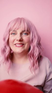 20 'li yaşlarda, kırmızı kalp hava balonuyla kameraya bakıp gülümserken selfie çekilen pembe arka plan, insanların yaşam tarzı kavramları.