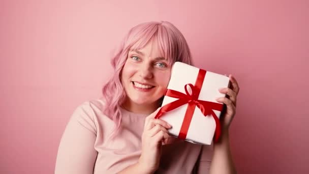 Celebration. Happy positive young caucasian woman showing gift box, while looking at camera isolated on pink background — Stock Video