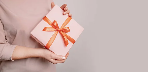 Kvinnliga händer håller överraskning presentförpackning presentera inslaget papper med band på pastell rosa bakgrund med kopieringsutrymme. 8 mars, födelsedag, mödradag — Stockfoto