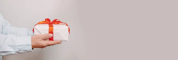 Primer plano de las manos de mujer sosteniendo caja de regalo sorpresa con lazo de satén rojo sobre fondo pastel rosa con espacio de copia. Regalo de San Valentín — Foto de Stock