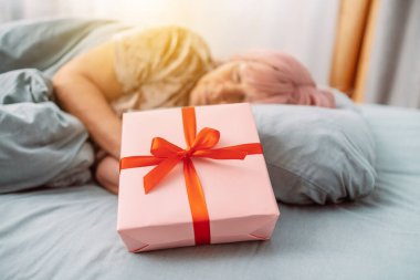 Kırmızı uyku maskeli kadın kırmızı saten kurdele desenli kağıt hediye kutusunun yanında uyuyor. Noel, Yeni Yıl, Sevgililer Günü ve doğum günü konsepti