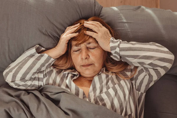 Mujer caucásica infeliz de mediana edad se siente mal con dolor de cabeza, migraña, estrés, insomnio después de despertarse en la cama por la mañana —  Fotos de Stock