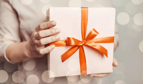 Női kéz kezében meglepetés ajándék doboz ajándék csomagolt papír piros íj pasztell rózsaszín háttér. Március 8., születésnap, anyák napja — Stock Fotó