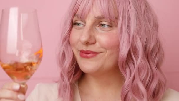 Красива 20-річна жінка з рожевим кучерявим волоссям, що п'є трояндове вино на яскраво-рожевому кольоровому фоні — стокове відео
