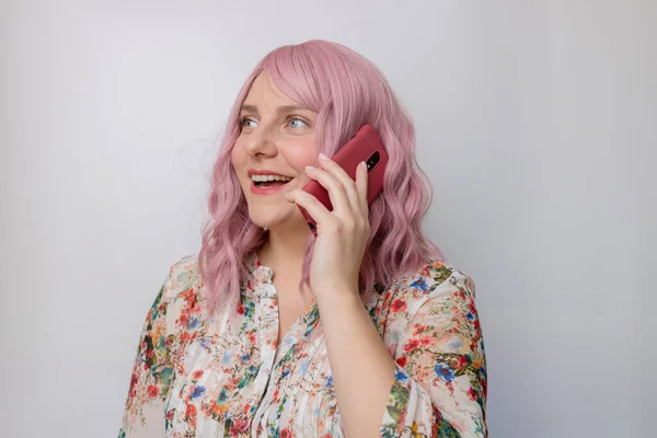 幸せな正ピンク巻き毛30代女性持っています電話会話上のライトグレーの背景スタジオ. — ストック写真