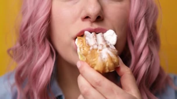 Κοντινό πλάνο του ελκυστικού χαρούμενα πεινασμένο οικογενειακό κορίτσι με ροζ χτένισμα των μαλλιών απολαμβάνοντας δάγκωμα νόστιμο γλυκό cupcake κρέμα απομονώνονται σε κίτρινο φόντο — Αρχείο Βίντεο