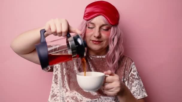 Aantrekkelijke mooie vrouwelijke hand houdt hete kop koffie drinken en theepot thee blik op camera genieten van zonnige ochtend geïsoleerd over roze muur achtergrond. — Stockvideo