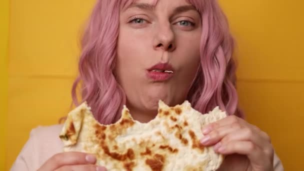 Крупним планом смішна щаслива голодна позитивна дівчина їсть хліб піти з сирною начинкою на жовтому фоні — стокове відео