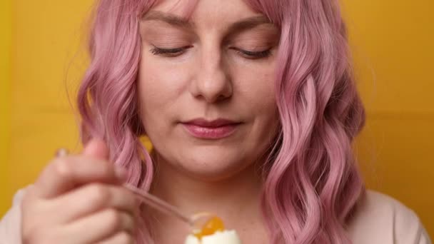 Closeup of attractive young woman enjoying eating jammed chicken egg on yellow stele background — Stock Video