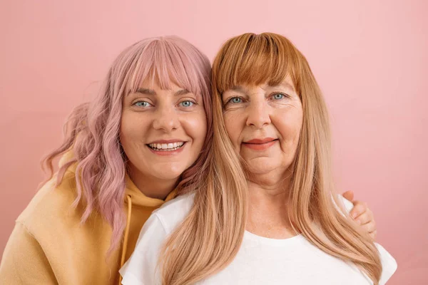Portret starszej matki i córki uśmiechniętych i przytulonych razem na różowej pastelowej ścianie. — Zdjęcie stockowe