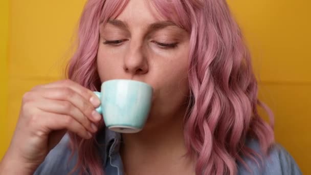 Portret van vrolijke jonge vrouw met roze haar kapsel genieten van een kopje koffie geïsoleerd over gele achtergrond — Stockvideo
