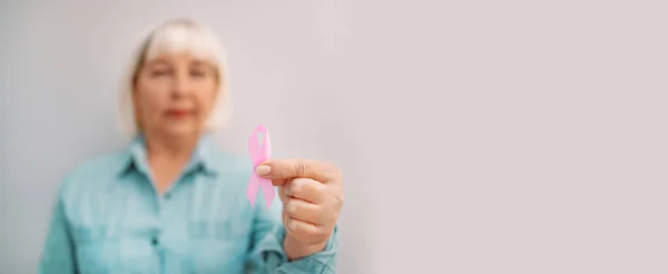 Blurred sonriente mujer caucásica de los años 50 en una camiseta con una cinta de satén rosa en la mano con espacio para copiar. Concientización sobre el cáncer de mama. Concepto de apoyo al cáncer de mama —  Fotos de Stock