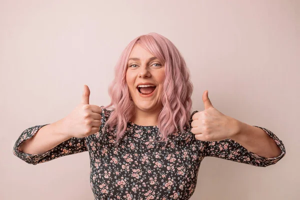Banner de promoções de atenção. Encantadora jovem mulher caucasiana com cabelo rosa em um belo vestido brilhante primavera mostrando polegar para cima como gesto isolado no fundo pastel — Fotografia de Stock