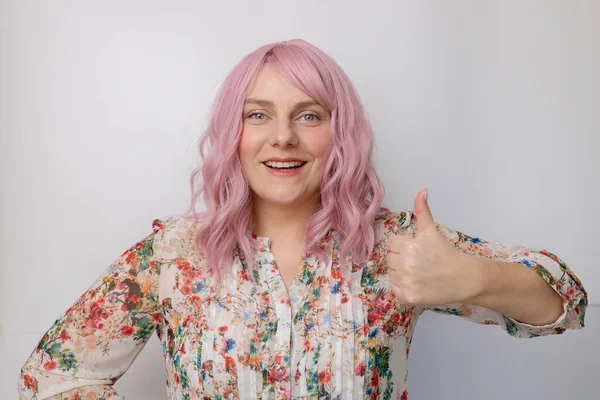 Encantadora jovem mulher caucasiana com cabelo rosa em um belo vestido brilhante primavera mostrando polegar para cima como gesto isolado no fundo pastel — Fotografia de Stock