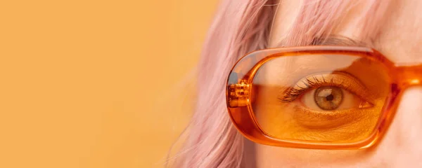 Hermosa joven con gafas de sol naranjas frescas sobre fondo amarillo. Primer plano del ojo de la mujer — Foto de Stock