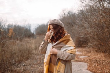 Alerji semptomu olan bir kadın soğuk bir sonbahar gününde burnunu dışarı sümkürdü..