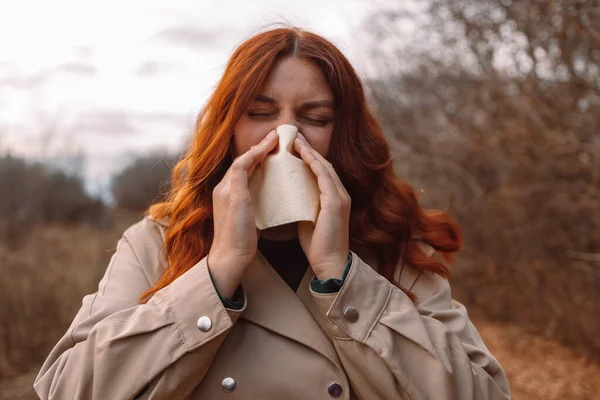 Soğuk bir sonbahar gününde mendili akan hasta bir genç kadın soğuk burun enfeksiyonu. Sağlık, soğuk, alerji konsepti