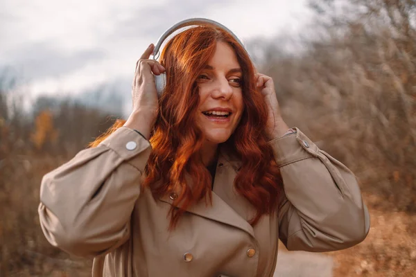 Joyeux rire femme bouclée cheveux écouter de la musique avec smartphone et écouteurs sans fil au parc de la ville — Photo