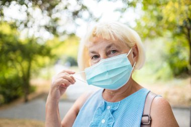 Coronavirus salgını sırasında nefes almak ve özgür hissetmek. 60 'ların 50' li yaşlarındaki kadın koruyucu maskesini çıkarıyor. Sağlık hizmetleri kavramı.
