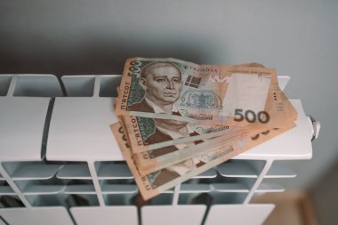 Hryvnia para banknotları evdeki ısıtma radyatörü bataryasında. Pahalı ısıtma masrafları. Faturaları ödüyorum.