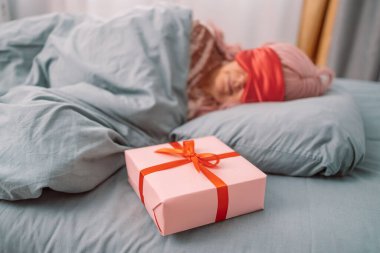 Kırmızı uyku maskeli kadın saten kurdele desenli kağıt hediye kutusunun yanında uyuyor. Noel, Yeni Yıl, Sevgililer Günü ve doğum günü