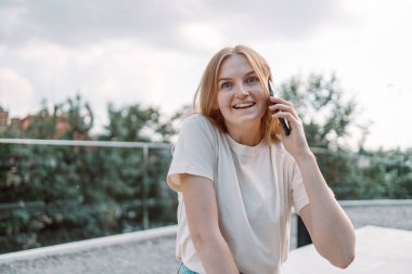 Açık havada telefonla konuşan gülümseyen bir kızın fotoğrafı.
