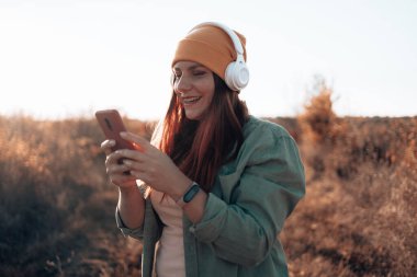 Günbatımı gökyüzü soyut arkaplanı ile akıllı telefon kullanan mutlu kadın.