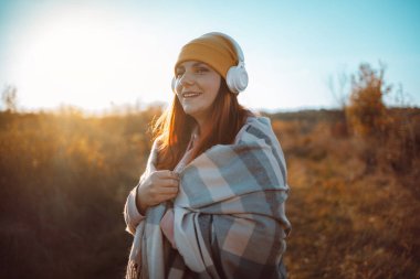 Parlak sarı örgü şapkalı, bej renkli eşarplı, mutlu bir şekilde gülümseyen, kulaklıklardan müzik dinleyen, çayırda yürümeyi seven 30 'lu yaşlardaki beyaz kadın.