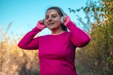 Beyaz kablosuz kulaklıklı aktif spor kadın doğadaki orman parkında koşuyor.