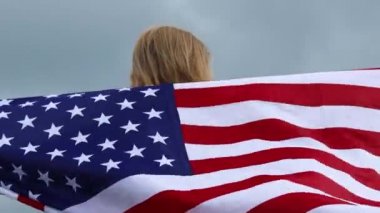 Amerika Birleşik Devletleri bayrağıyla mutlu bir kadın gün batımı arka planında dağın tepesinde güzel doğa manzarasının tadını çıkarıyor. Mutlu tatiller.