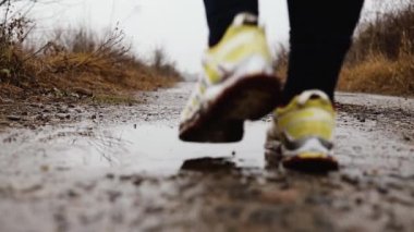 Spor ayakkabısı giyen bir kadın sonbaharda su sıçratarak koşuyor ve zıplıyor.